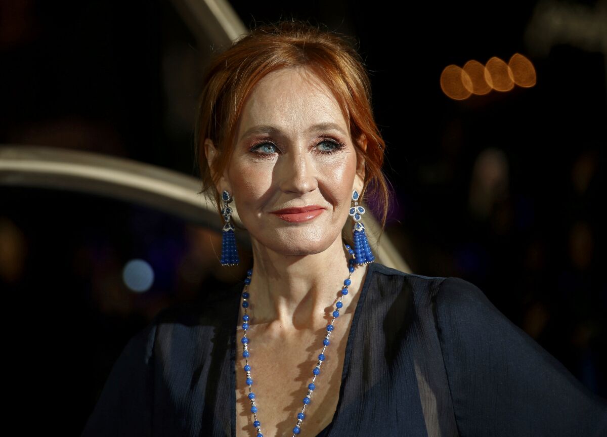 A red-haired woman with a beaded necklace and earrings poses at a movie premiere. 
