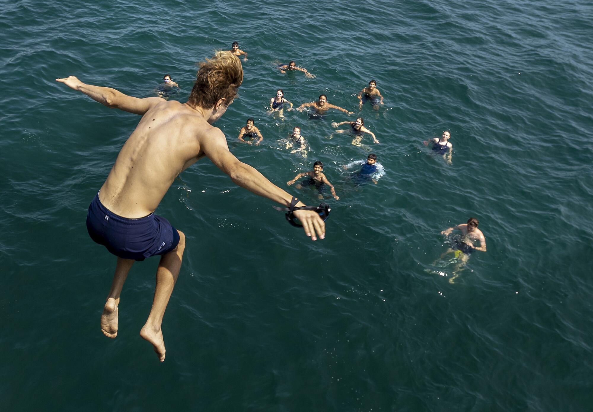 A teenager jumps into the ocean where a group of people tread water