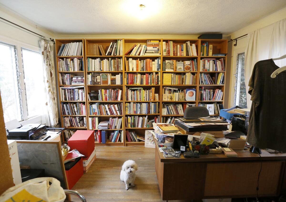 Paco sits in front of Evan Kleiman's elaborate cook book collection. Kleiman is downsizing from a spacious apartment to a compact 500 square feet and she has a lot of cookbooks.