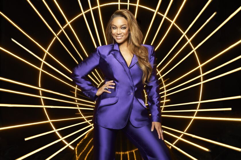 Tyra Banks in a sleek purple suit against a bright background