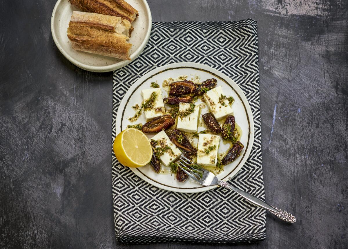 One plate of sauteed dates and feta with half a lemon and a smaller plate with some baguette