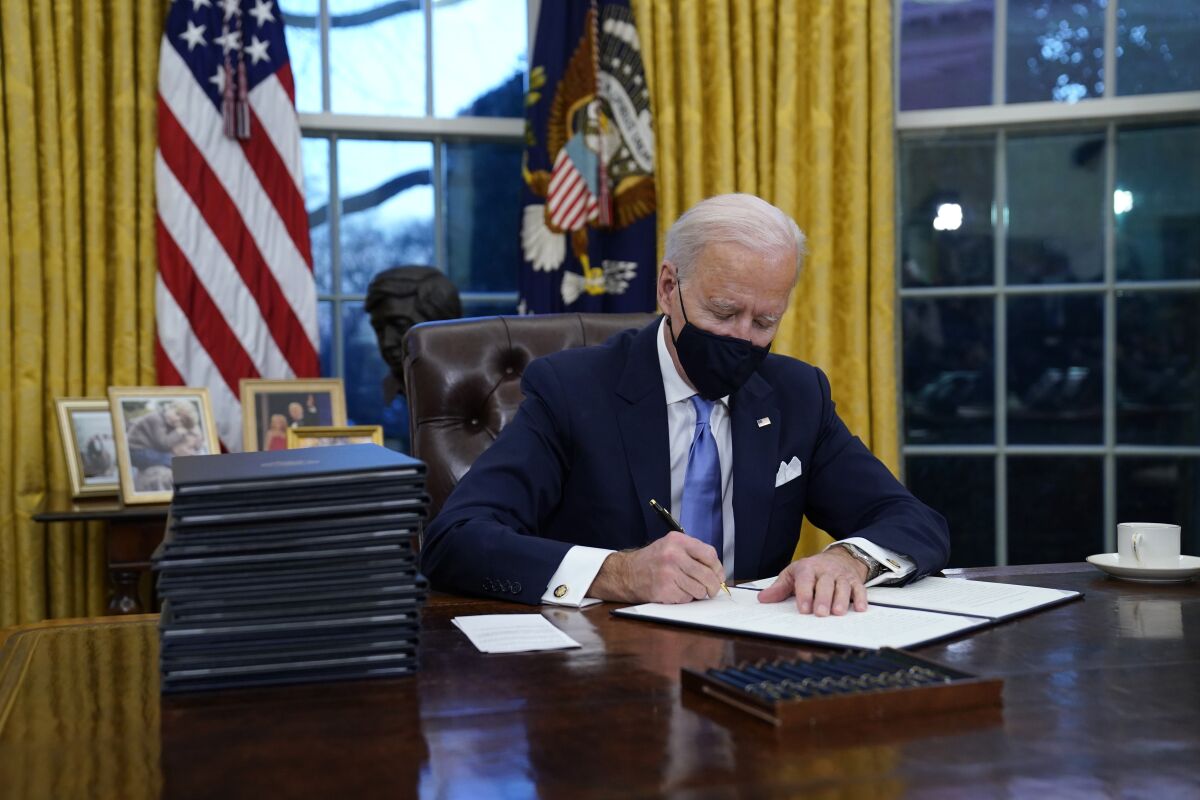 FILE - In this Jan. 20, 2021, file photo, President Joe Biden signs his first executive order in the Oval Office of the White House in Washington. Biden laid out an ambitious agenda for his first 100 days in office, promising swift action on everything from climate change to immigration reform to the coronavirus pandemic. Key members of the White House Environmental Justice Advisory Council say one year into the Biden Administration's commitment that 40% of all benefits from climate investment go to disenfranchised communities, not enough has been done. (AP Photo/Evan Vucci, File)