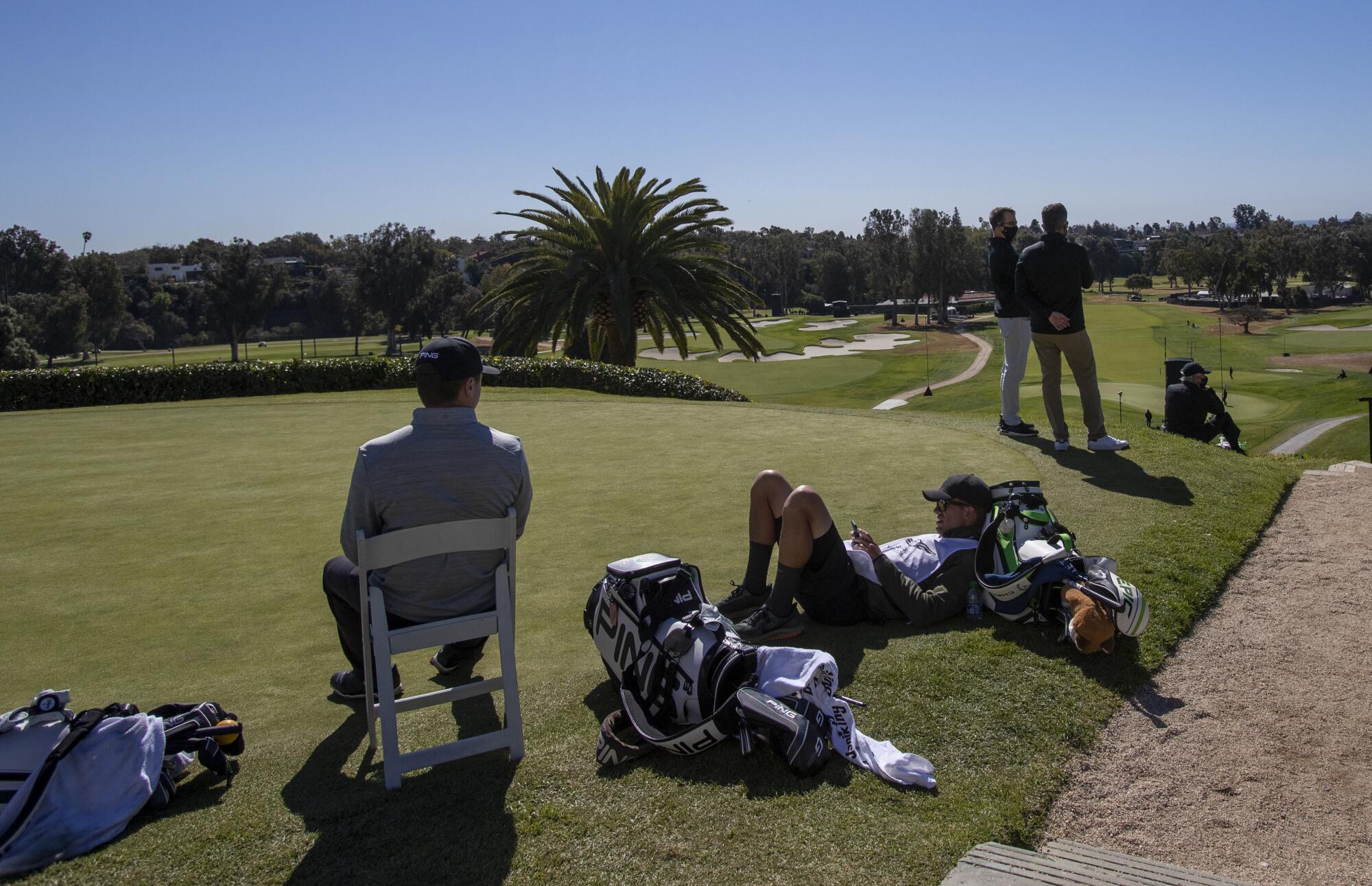 Golfers and their caddies relax on a tee box