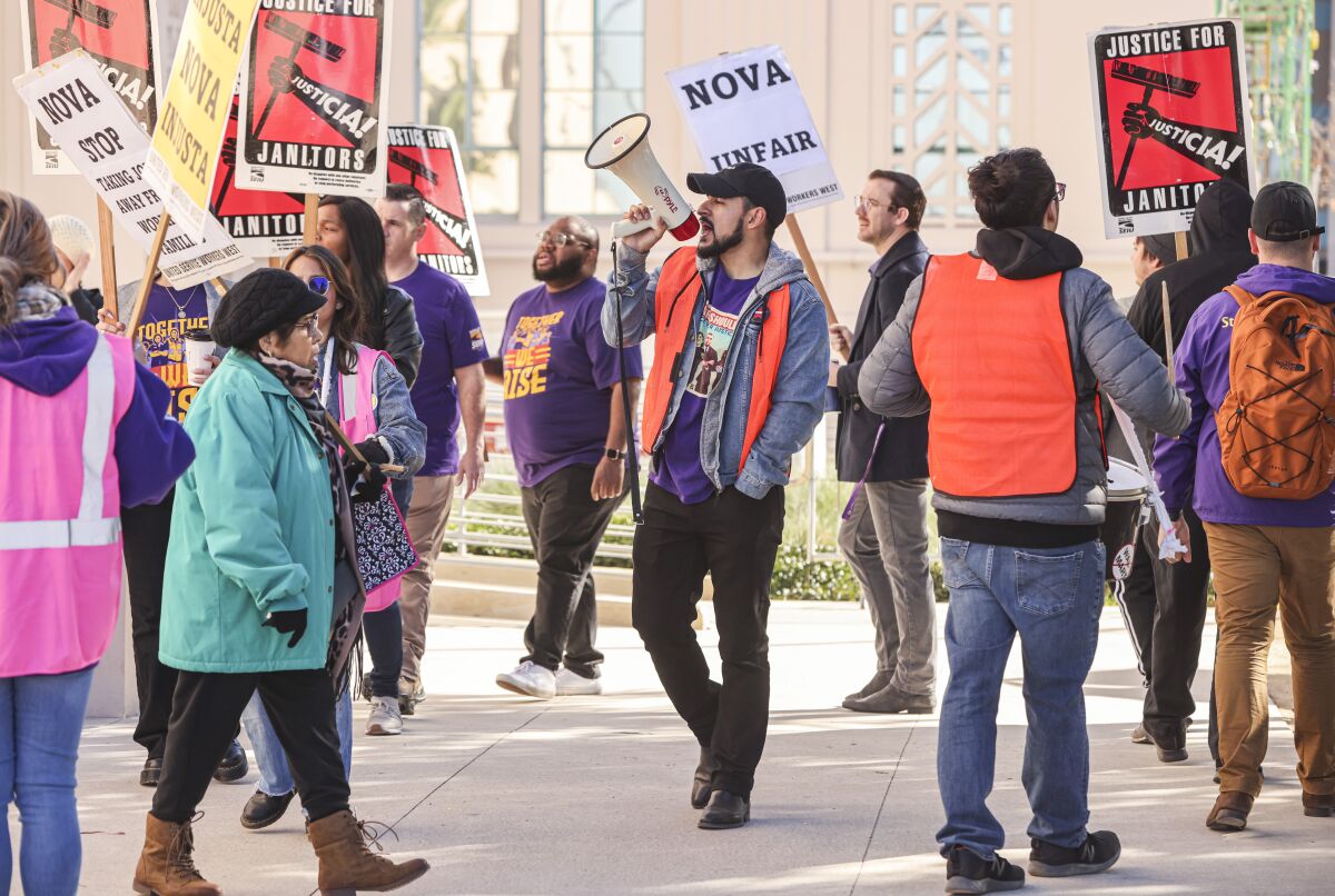 Strikers wearing safety vests and purple T-shirts picket, carrying signs saying "Nova Unfair" and "Justice for janitors."