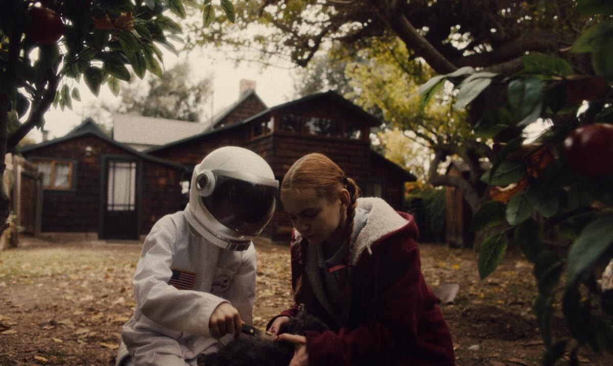 Two children, one dressed as an astronaut, play in a yard.