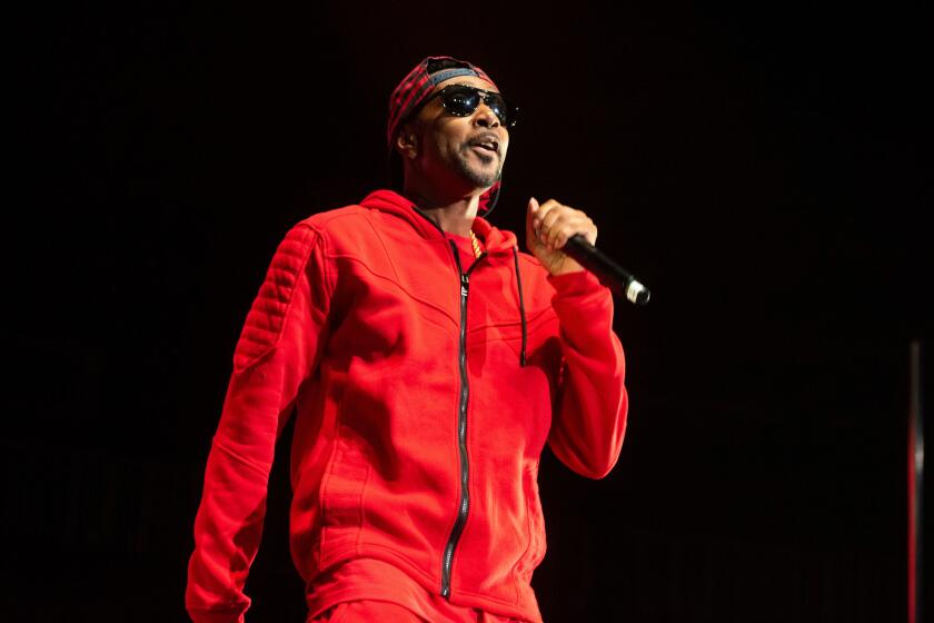 Krayzie Bone stands on a darkened stage in a red tracksuit, dark glasses and backward cap and raps into a microphone