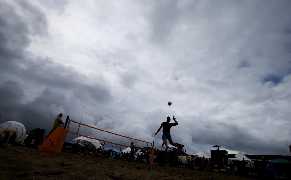 A beach volleyball player leaps to make a serve under stormy skies during the AVP Huntington Beach Open.
