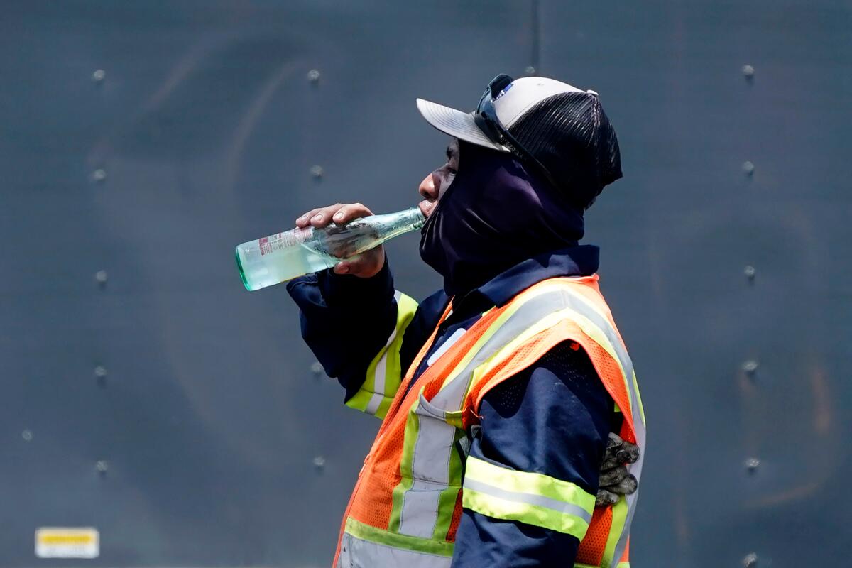 Framed waist-up in profile, a man wearing high-visibility vest, a hood and a cap, drinks water from a bottle