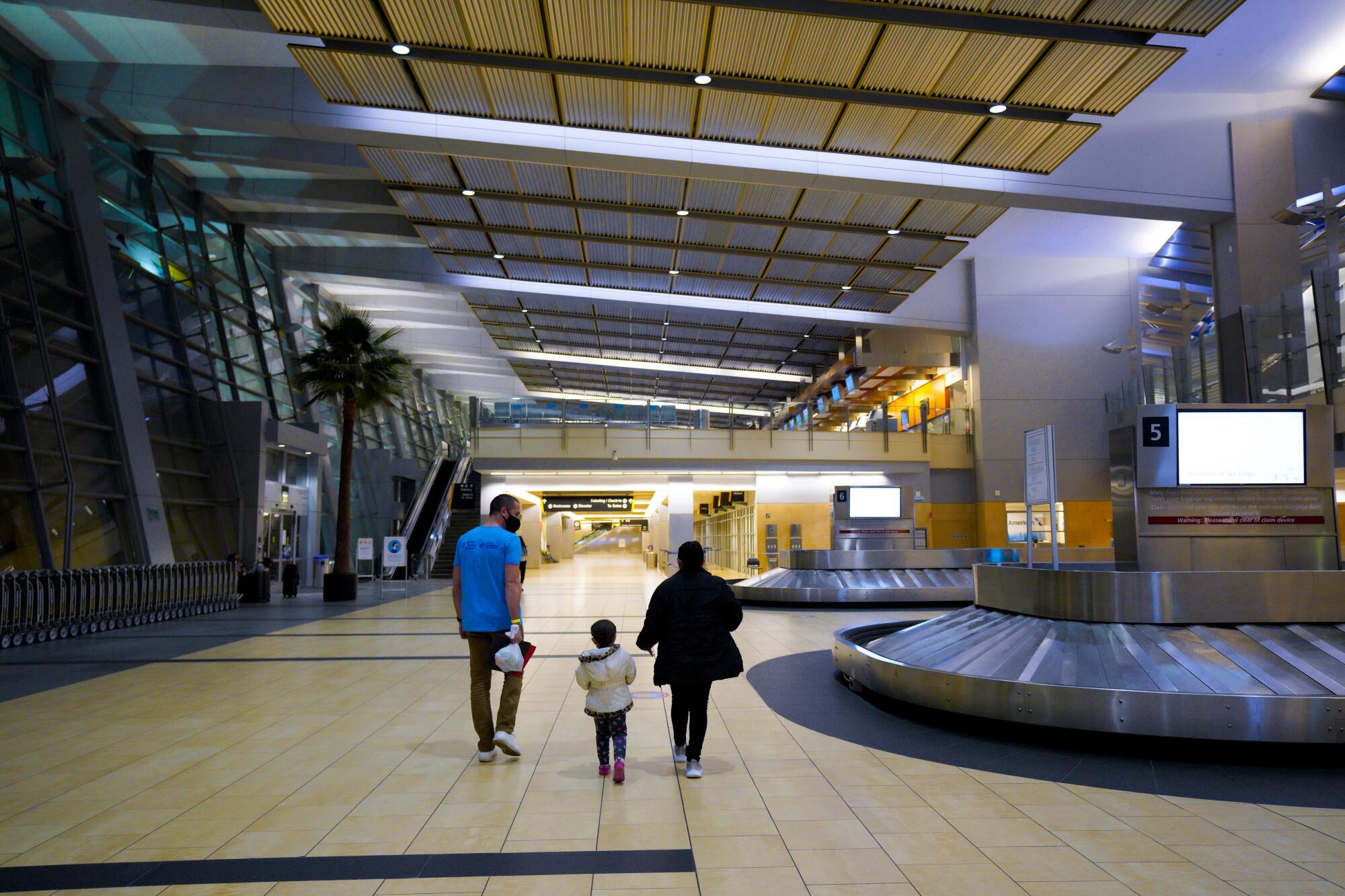 A man, woman and child walk beside an airport luggage carousel.