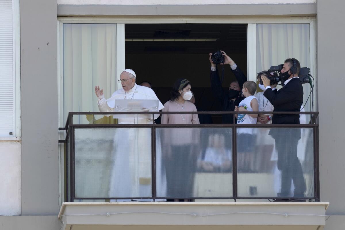 Francis stands with children and a cameraman on a balcony.