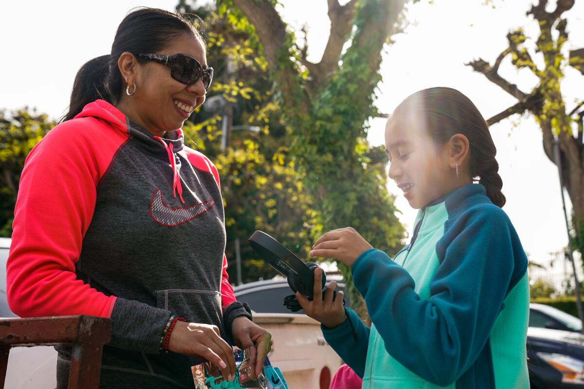 Gaby Regalado and daughter Yuliana, 8, check out Yuliana's donated headphones, which should help her study at home, while her family picks up food at the Mar Vista Family Center. Yuliana especially likes the coffee cake.
