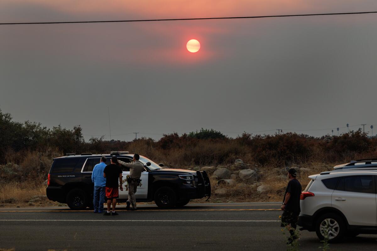 With the backdrop of a smoky sunset, a CHP officer advises residents at a road block on Highway 38.