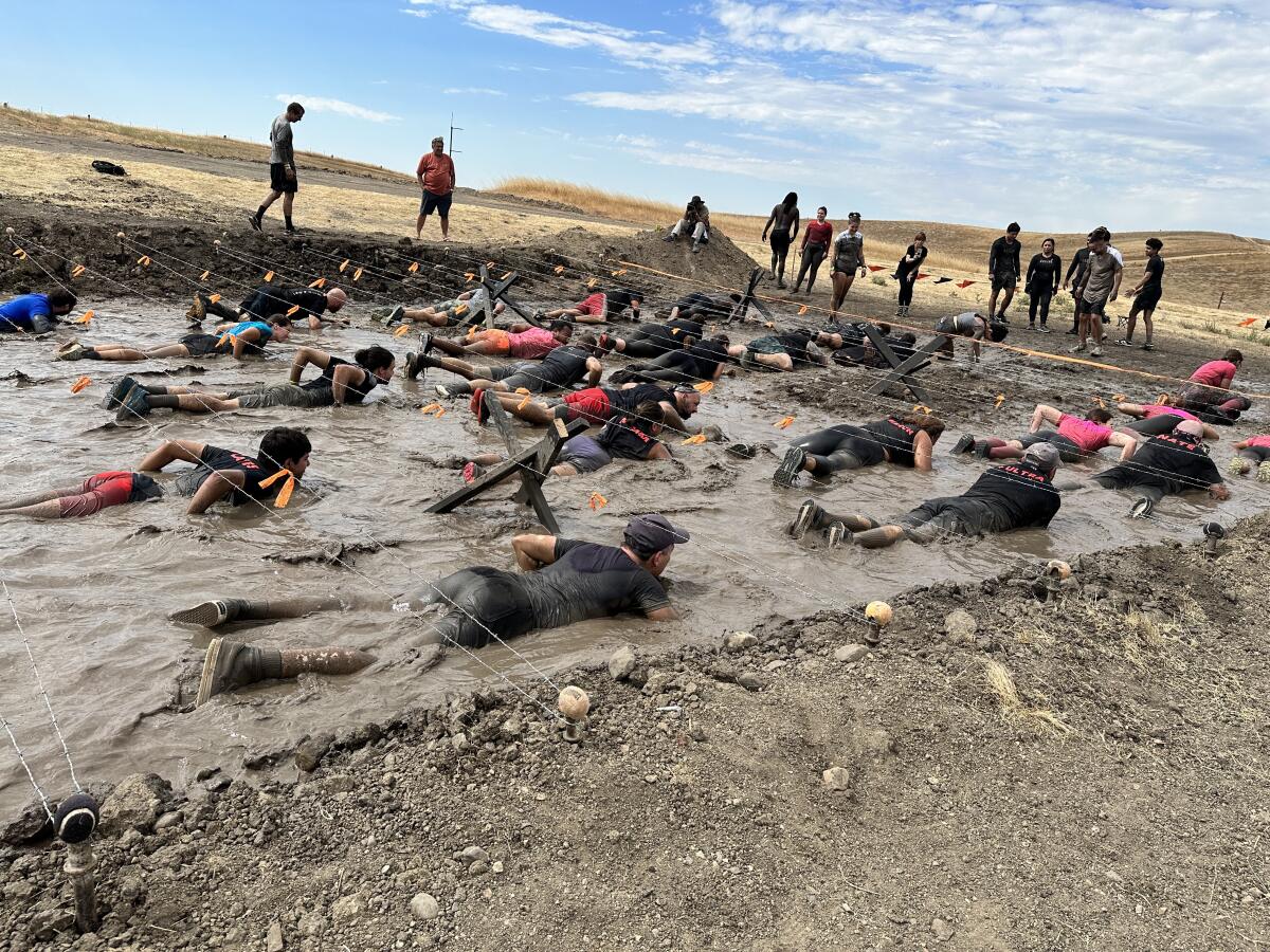 People lie on their bellies in muddy water in a dirt field.