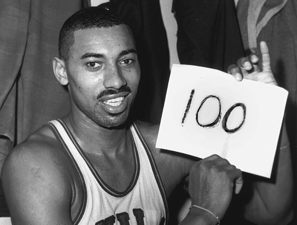 FILE - Wilt Chamberlain, of the Philadelphia Warriors, holds a sign reading "100" in the dressing room in Hershey, Pa., March 2, 1962, after he scored 100 points, as the Warriors defeated the New York Knicks. Wednesday marks the 60th anniversary of the greatest scoring effort in NBA history — 36 field goals, 28 free throws, 100 points for Chamberlain, in the Warriors’ 169-147 win in a game played before about 4,000 people in Hershey. It might be the closest thing the NBA has to a single-game record that will never be broken. (AP Photo/Paul Vathis, File)