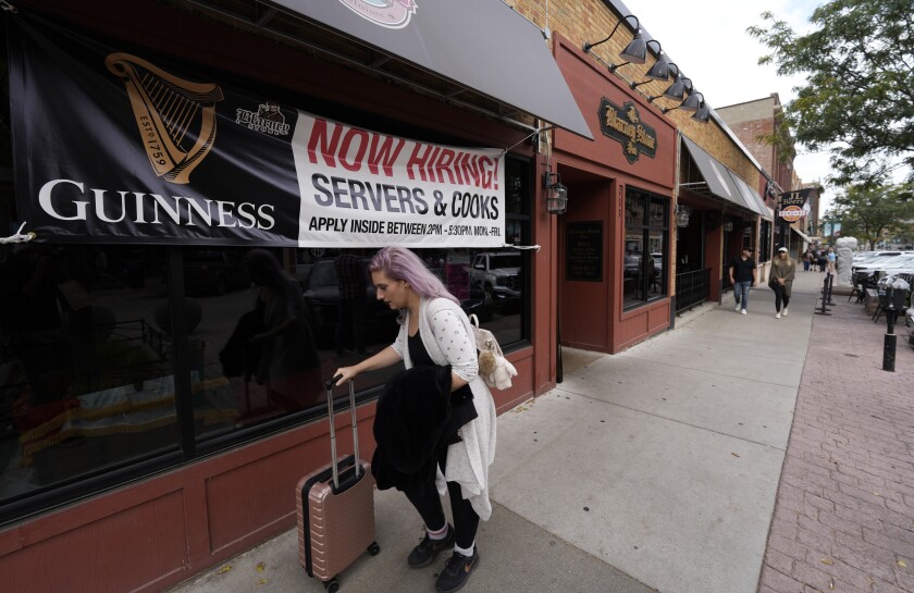 FILE - A traveller wheels her baggage past a now hiring sign outside a bar and restaurant Saturday, Oct. 9, 2021, in Sioux Falls, S.D. America’s employers slowed the pace of their hiring in November, adding 210,000 jobs, the lowest monthly gain in nearly a year. Friday, Dec. 3 report from the Labor Department also showed that the nation's unemployment rate tumbled from 4.6% to 4.2% evidence that many more people reported that they had a job. (AP Photo/David Zalubowski)