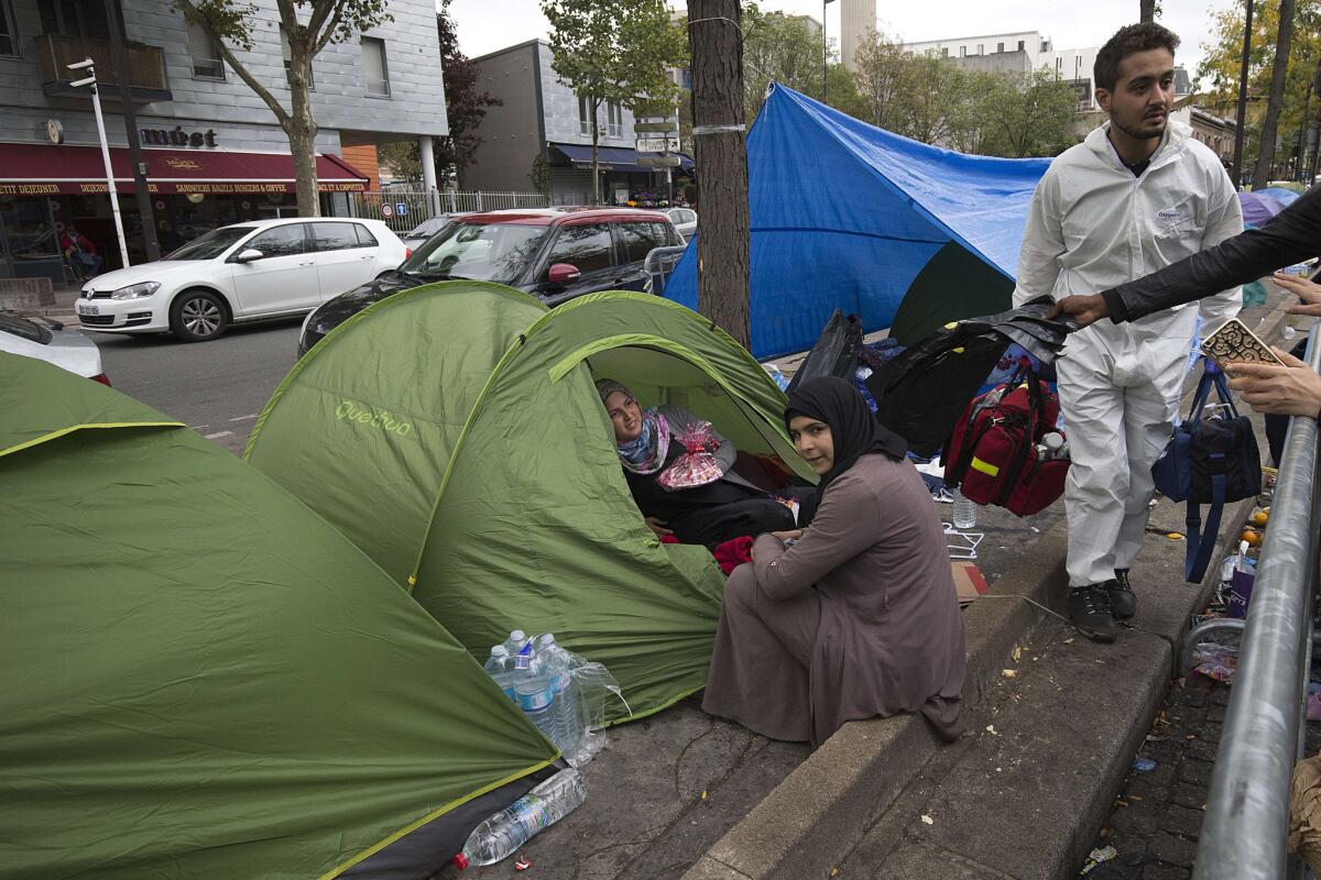 A volunteer passes Syrian refugees as he tours a makeshift camp at Porte de Saint-Ouen, in northern Paris, where some 60 migrant families settled near a highway.
