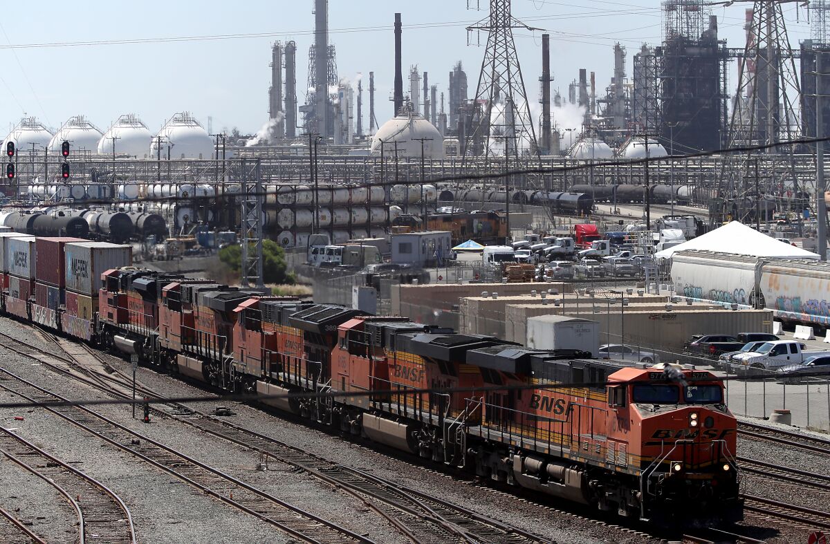 A freight train moves past an oil refinery in the Port of Los Angeles.