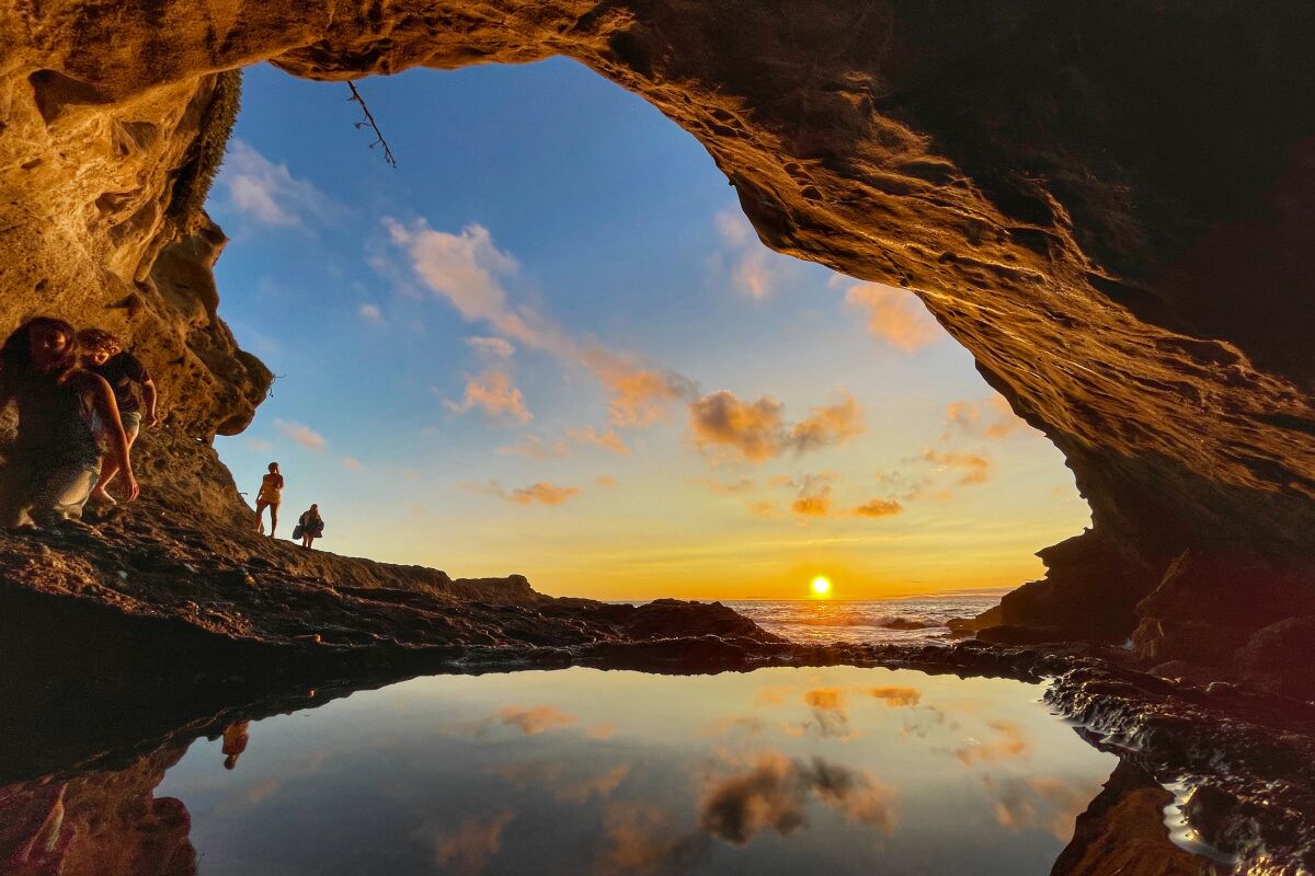The sun sets into the ocean, framed by a sea cave entrance.