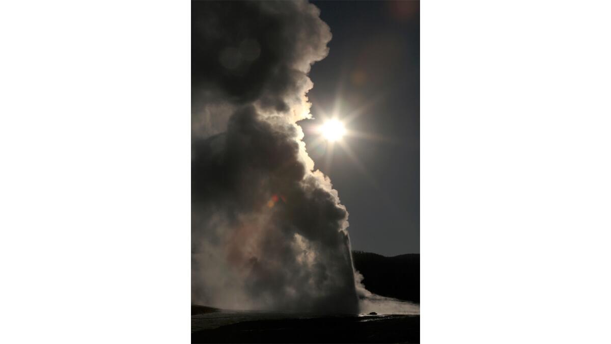 The sun rises behind a plume of smoke and steam from the Old Faithful geyser in Yellowstone National Park.