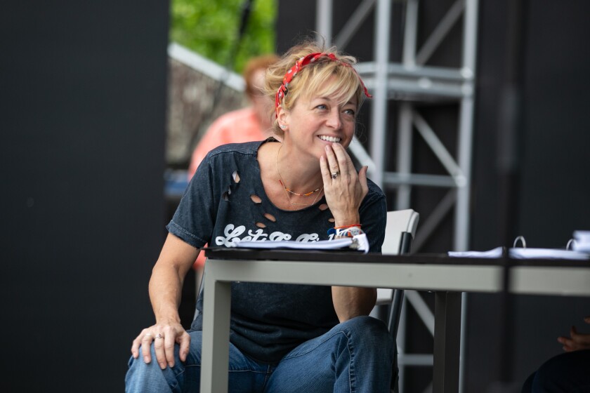 A woman in a blue T-shirt and jeans is sitting at a table with a script.