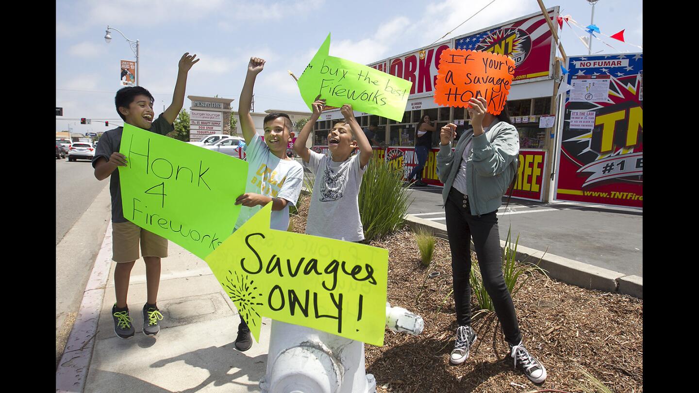 Armando Silva, Hector Sanchez, Victor Sanchez, and Delaney Novoa, from left, cheer at honking cars to bring attention to their TNT fireworks booth during the first day of "safe and sane" fireworks sales in Costa Mesa on Friday.