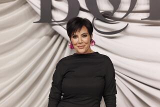 Kris Jenner poses in a black dress and floral earrings in front of a white draped backdrop