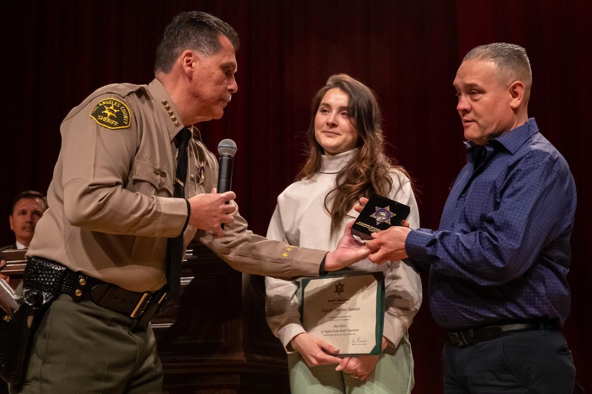 Sheriff Robert Luna presents a service badge for Alejandro Martinez to his sister Dayanna Martinez and father Arturo Martinez