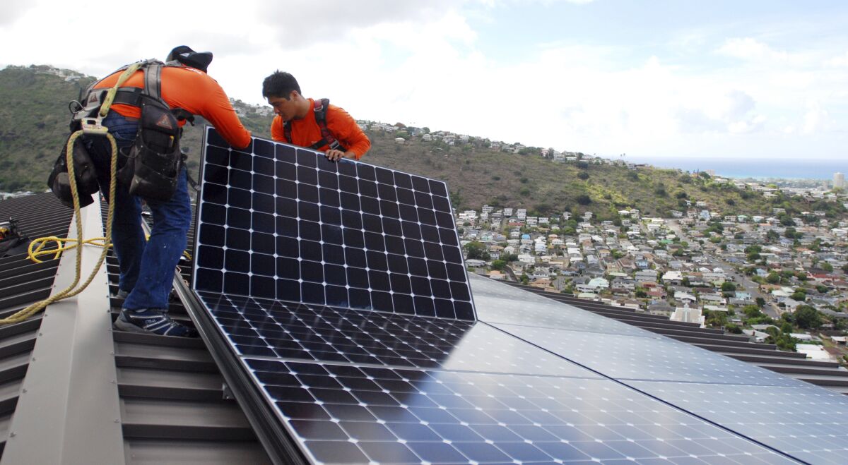 In this July 8, 2016, file photo, workers place solar panels on a roof.