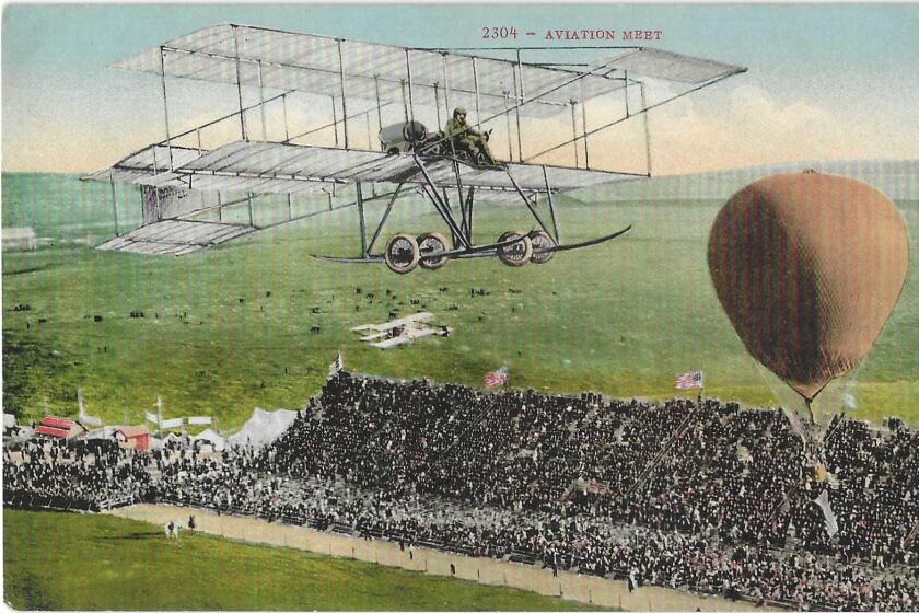 An airplane and an orange hot air balloon over a green field and a packed grandstand