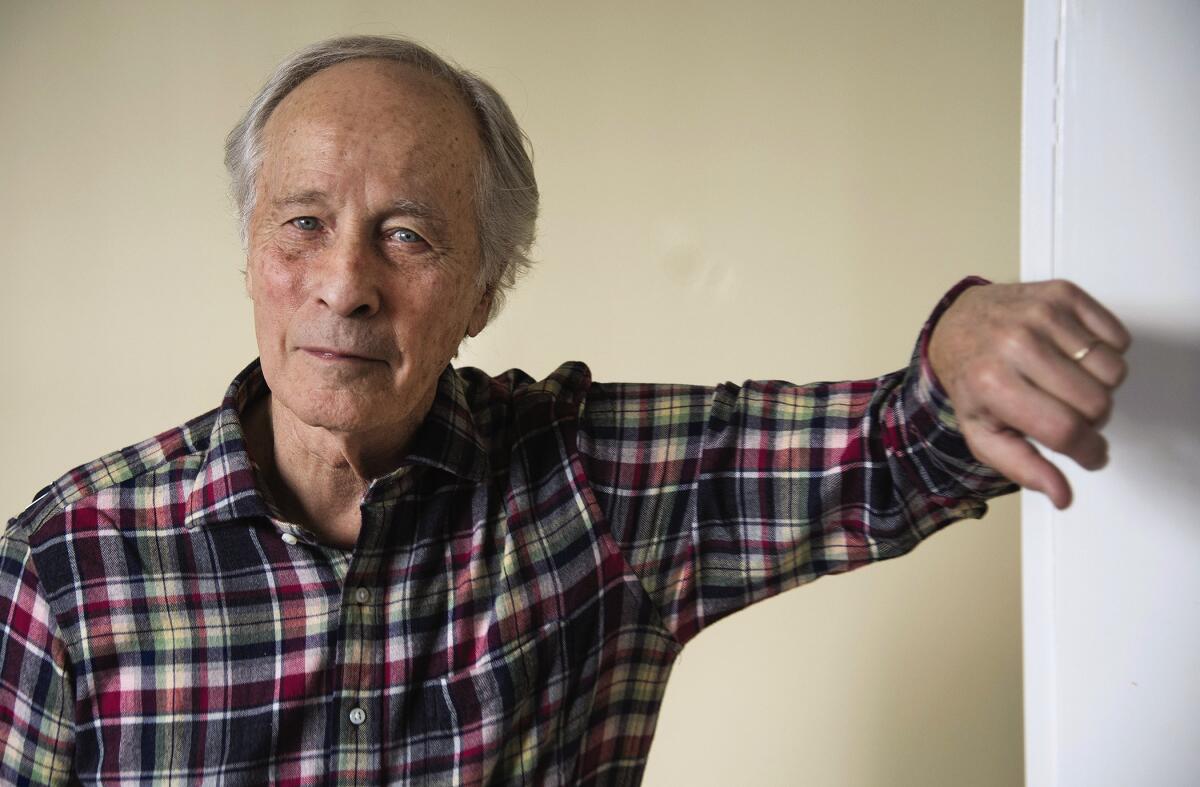 Richard Ford, wearing a plaid shirt, leans against a wall.