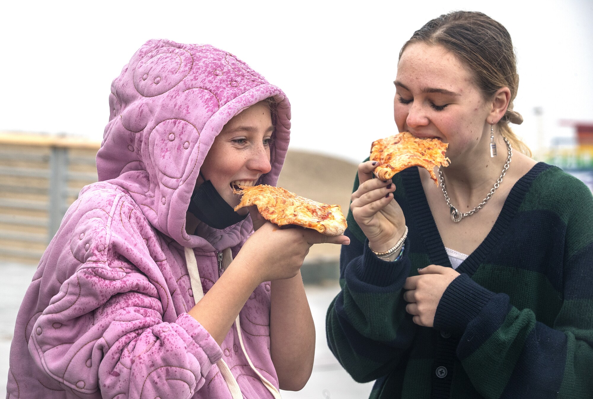 لیلی اسمیت، سمت چپ، و تیلور سلماس هنگام بازدید از ساحل هرموسا، از یک تکه پیتزا زیر باران لذت می برند.