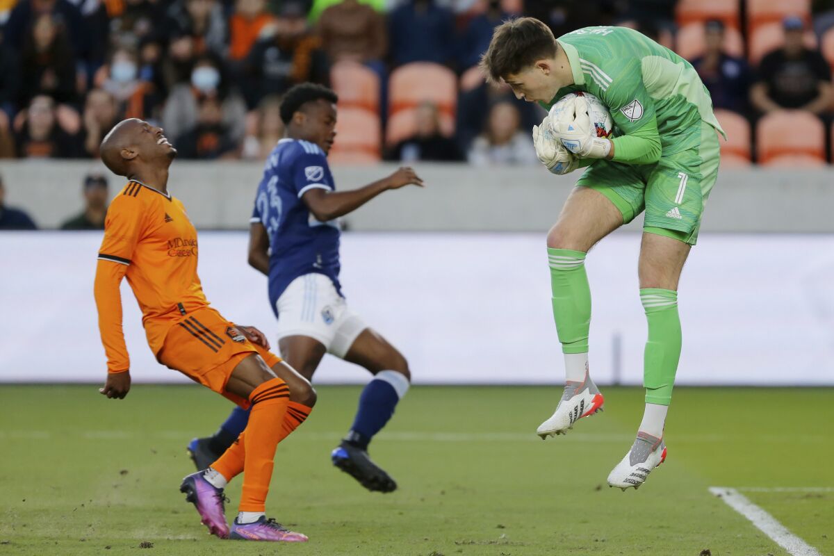 Houston Dynamo midfielder Fafà Picault, left, reacts next to Vancouver Whitecaps defender Javain Brown (23) as goalkeeper Thomas Hasal, right, makes a save during the first half of an MLS soccer match Saturday, March 12, 2022, in Houston. (AP Photo/Michael Wyke)
