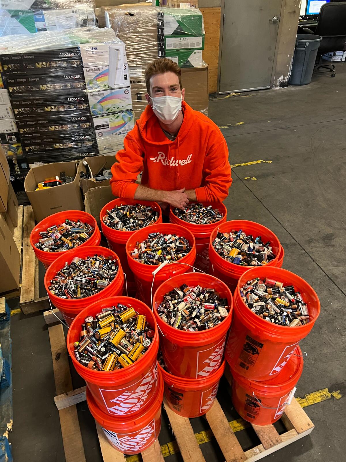 A Ridwell employee poses next to bins of batteries