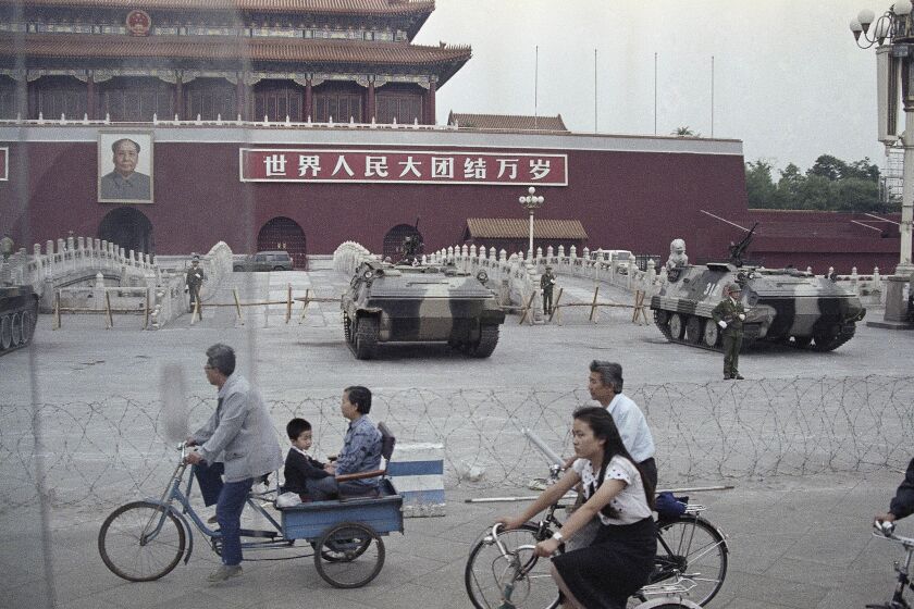 FILE - Cyclists pass by armored vehicles parked in front of Tiananmen Gate near the square where students rallied for democratic reforms in Beijing, June 13, 1989. An exhibit will open Friday, June 2, 2023, in New York, ahead of the June 4 anniversary of the violence that ended China's 1989 Tiananmen protests. (AP Photo/Sadayuki Mikami, File)