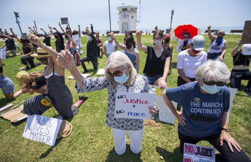 Margo Ganson, left, and Molly Pritchard kneel for nine minutes during a  protest at Main Beach in Laguna Beach on Wednesday.