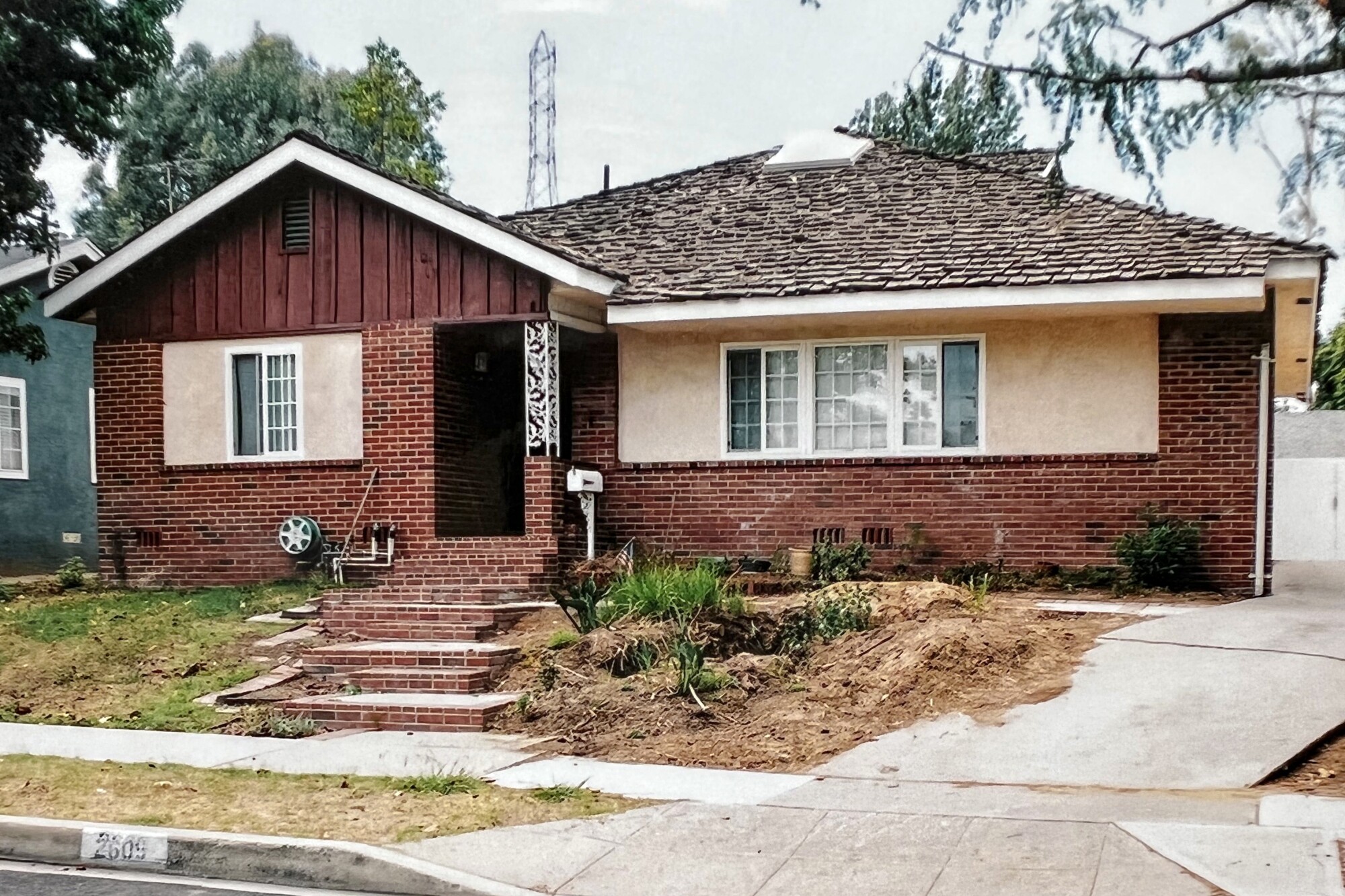 A brick house with steps and dying grass and a dirt patch with a few plants.