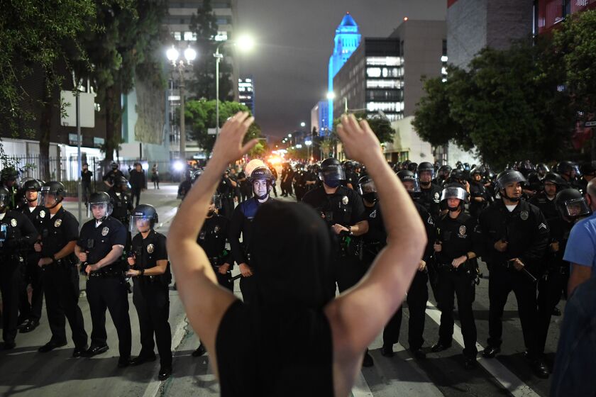 LOS ANGELES, CALIFORNIA MAY 29, 2020-A protestor raises his arms as LAPD officers approach on Spring St. in Downtown Los Angeles Friday. Protestors marches across the nation after the death of George Floyd. (Wally Skalij/Los Angeles Times)