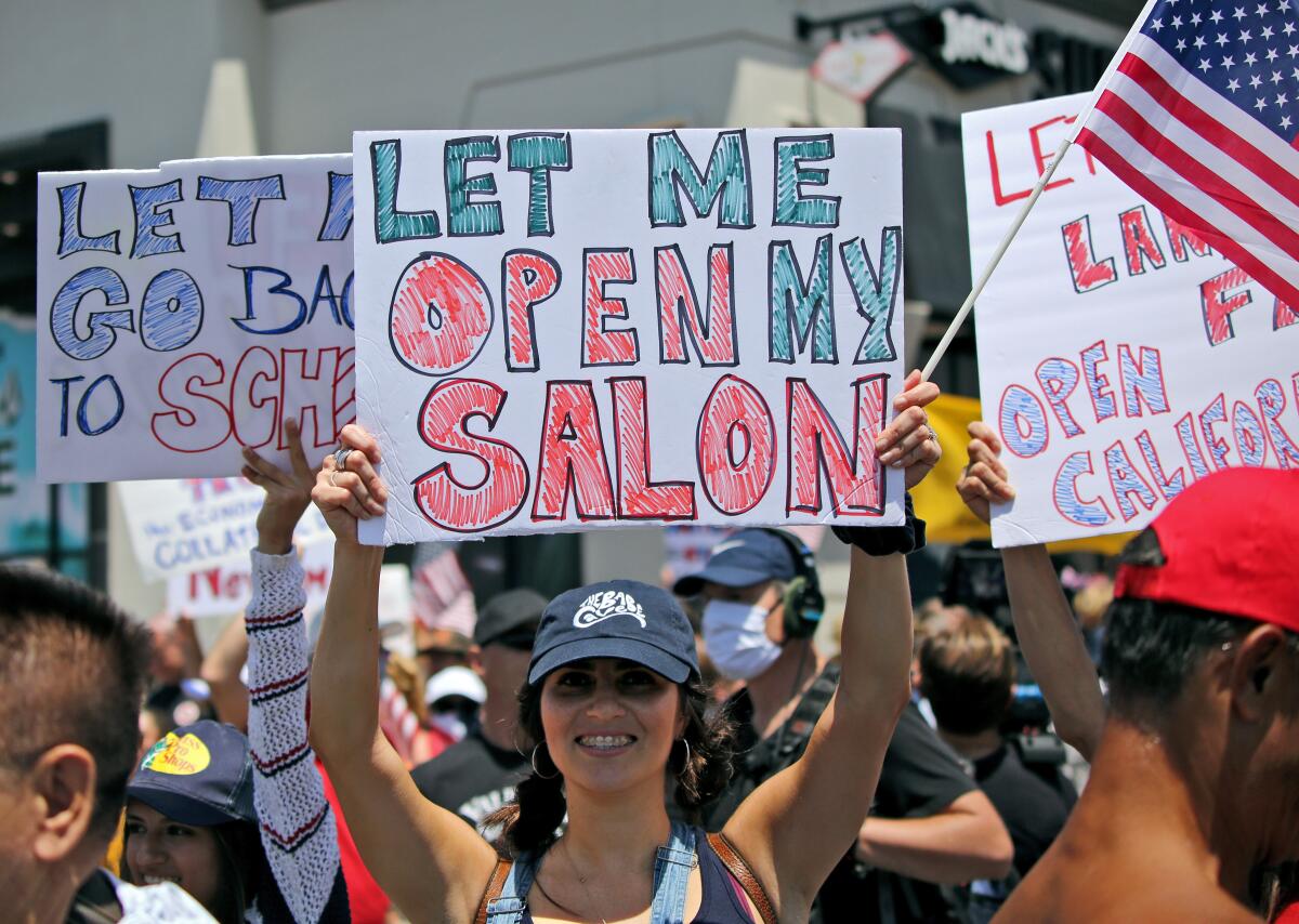 The Babe Cave Waxing and Skincare owner Haily Lemaster, of Upland, holds a sign up during the "Live Free Protest to Open CA." protest at Main and Pacific Coast Highway in Huntington Beach on May 1.
