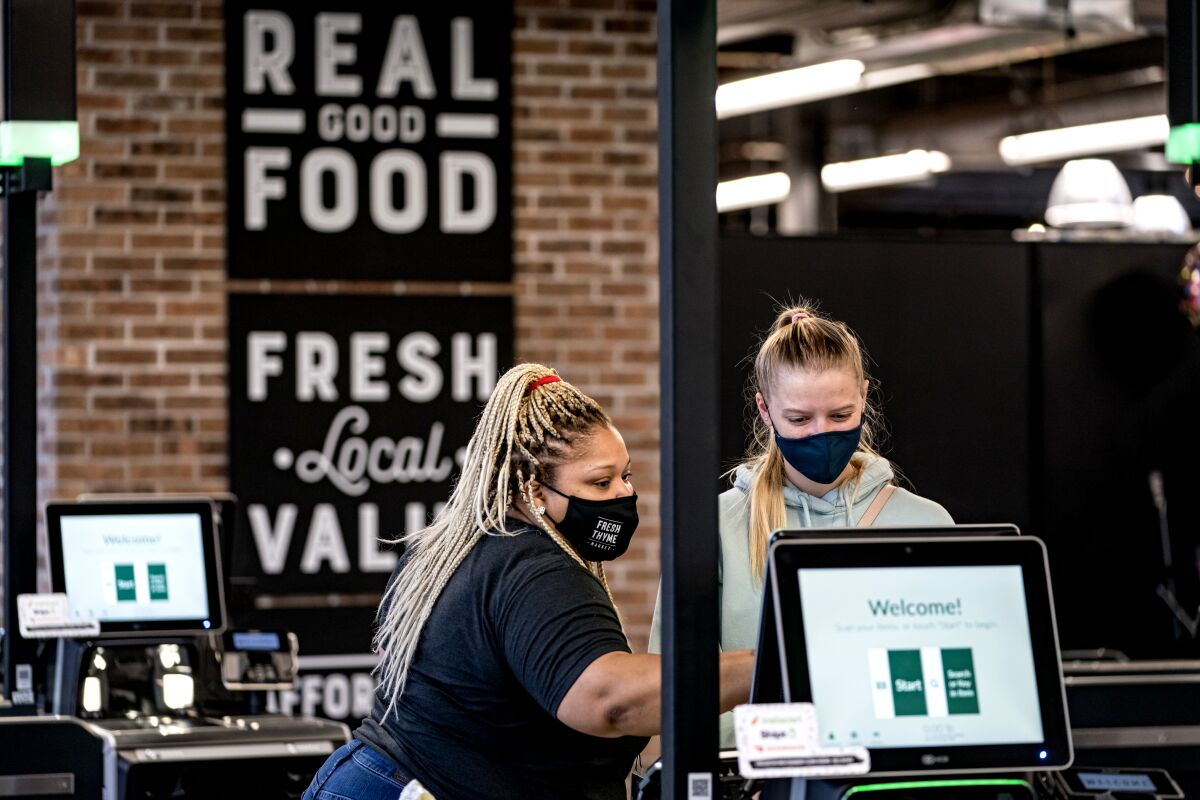 An employee assists a customer at a self-checkout machine.