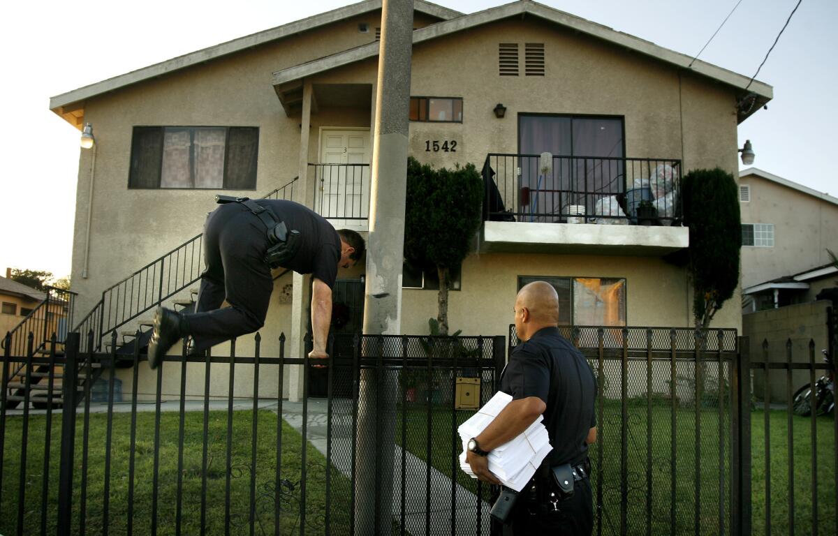 An LAPD officer jumps a fence to let his partner into a housing complex in 2007 while serving notice of a gang injunction. Illegal curfew provisions included in many of the city's gang injunctions were at the center of a federal class-action lawsuit.