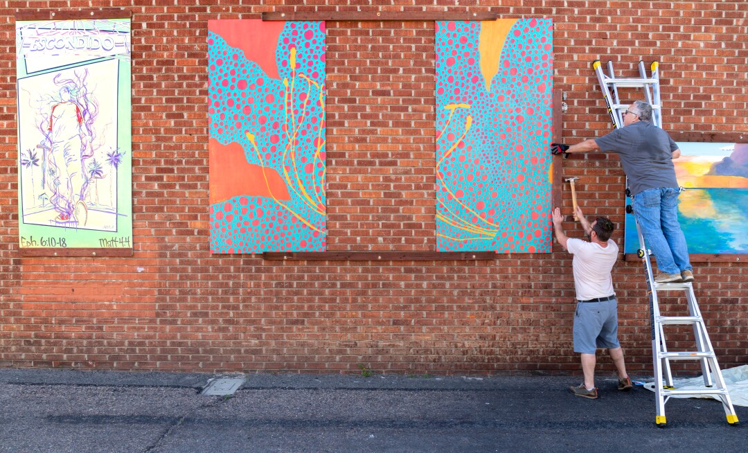 Escondido Art Association committee members Tristan Pittard and Dan Forster (on ladder) install artist mural panels
