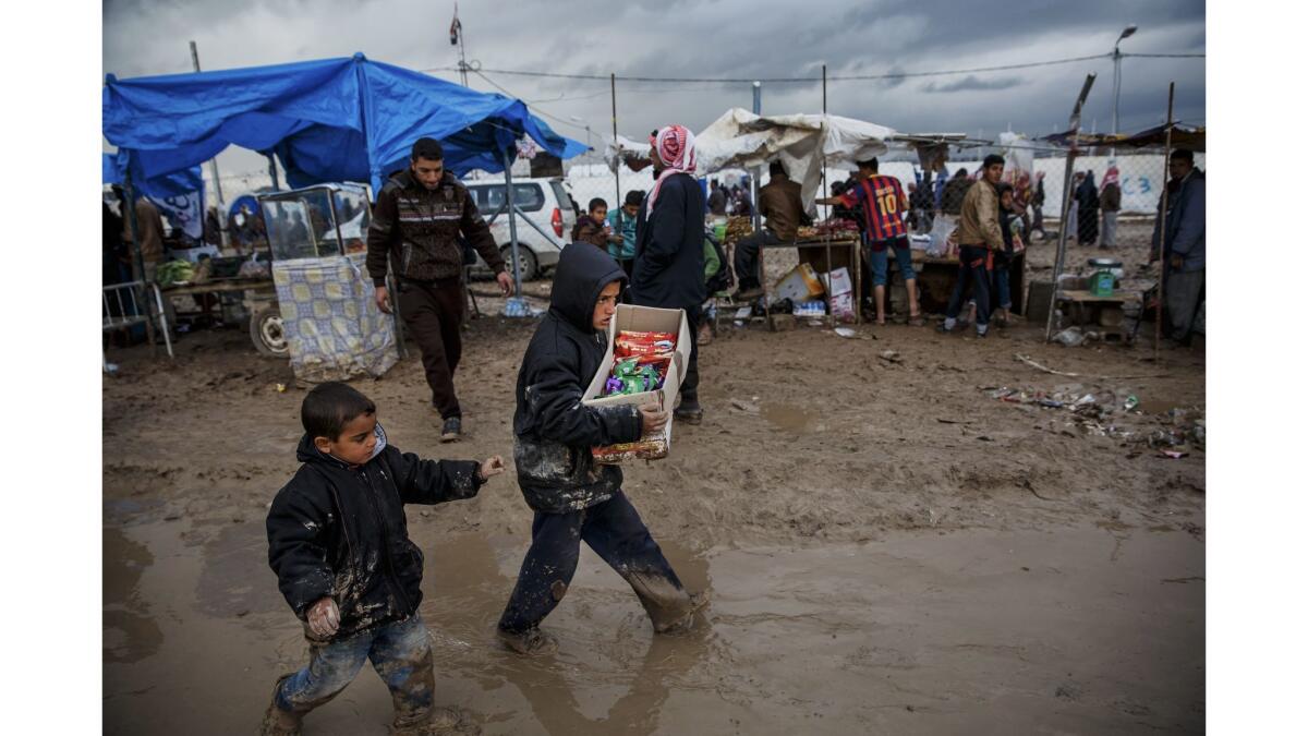 Two boys carry food back to their families in the muddy and flooded area outside the displaced persons camp in Hamam Alil, Iraq. The camp is already filled with an estimated 30,000 displaced residents of Mosul.