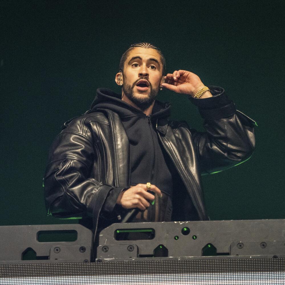 Bad Bunny adjusts his earpiece and holds a microphone while performing on a stage