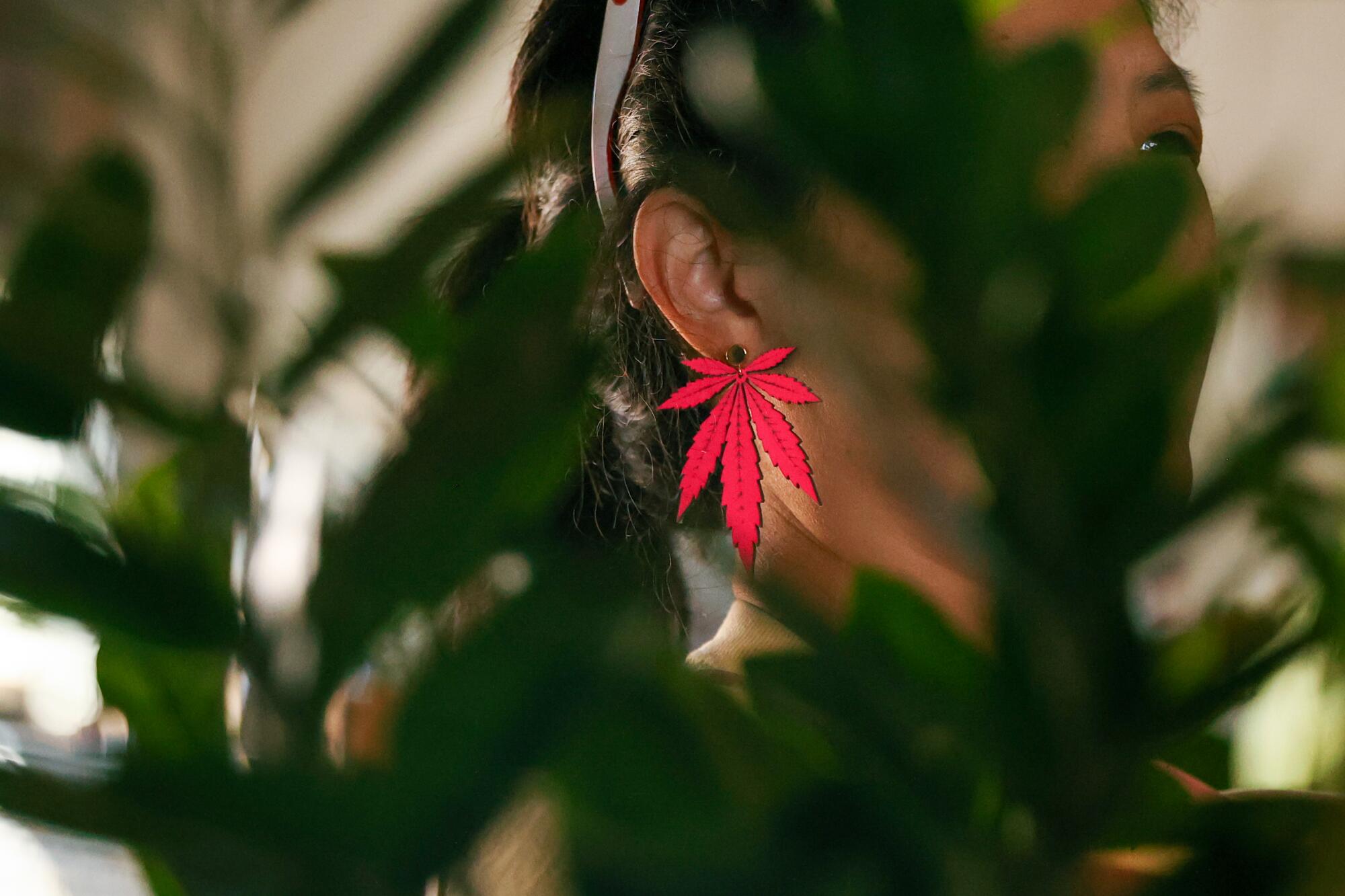 A woman wearing a red earring shaped like a marijuana leaf