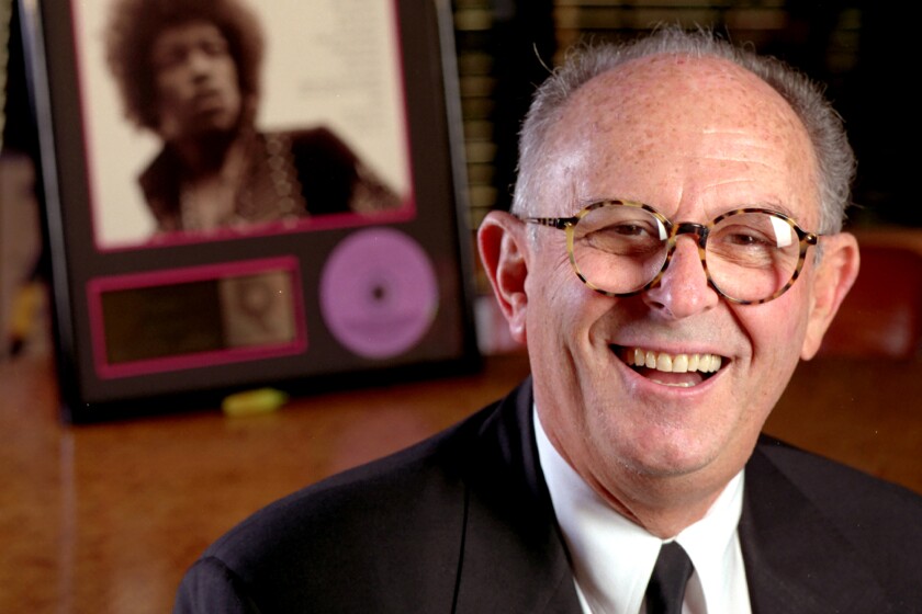 A record executive with glasses and short gray hair in front of a photo of Jimi Hendrix