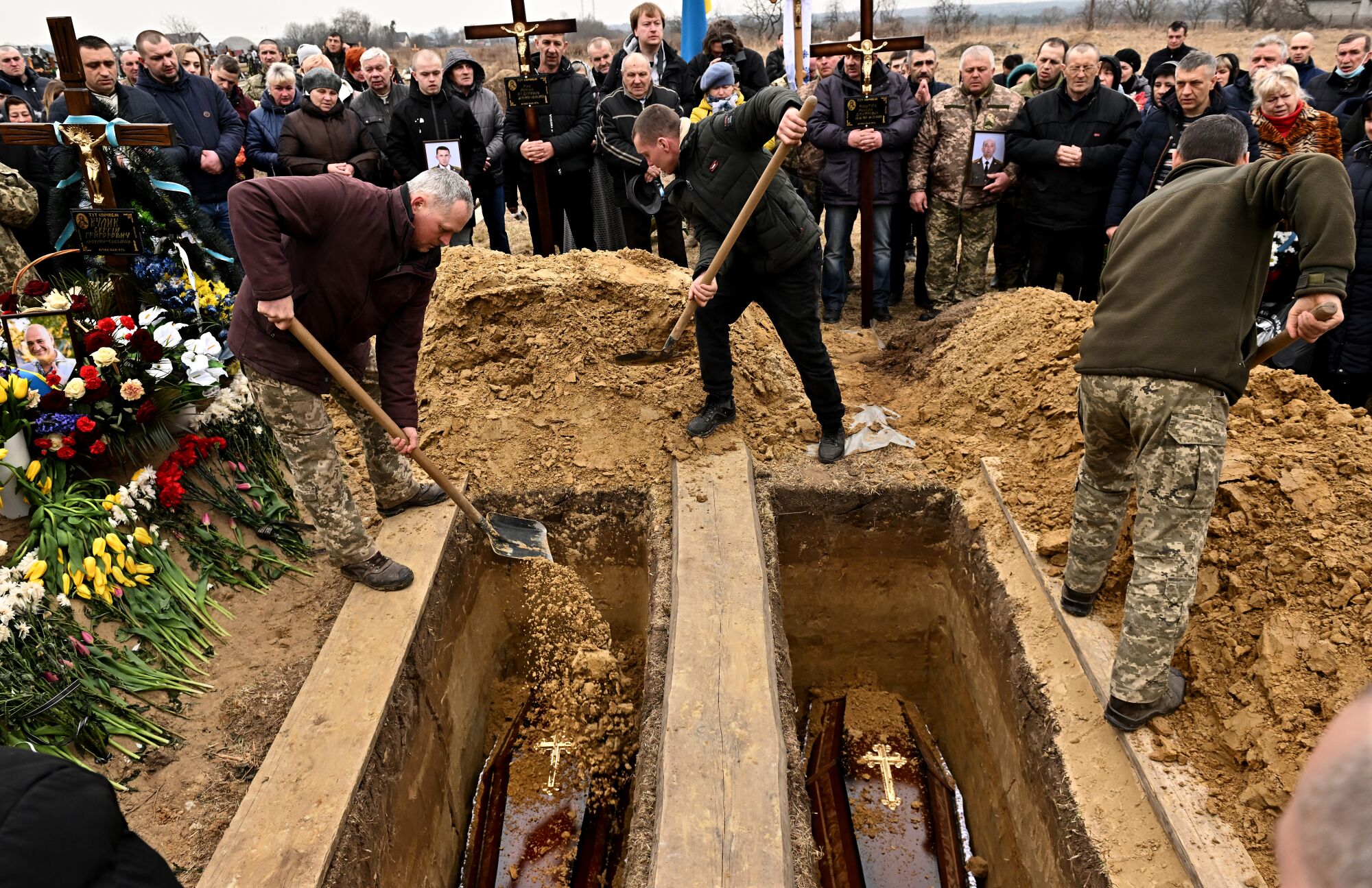 People shovel dirt into two graves.