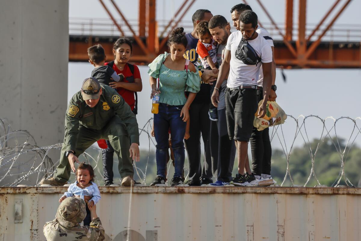 Migrants wait next to Border Patrol agents.