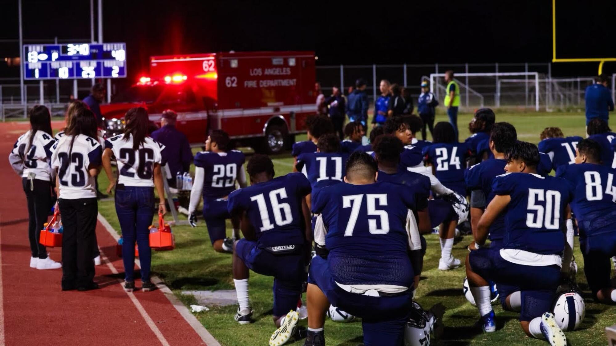 Varsity football players from Venice and Edison watch the ambulance carrying Nathan Santa Cruz exit the field.