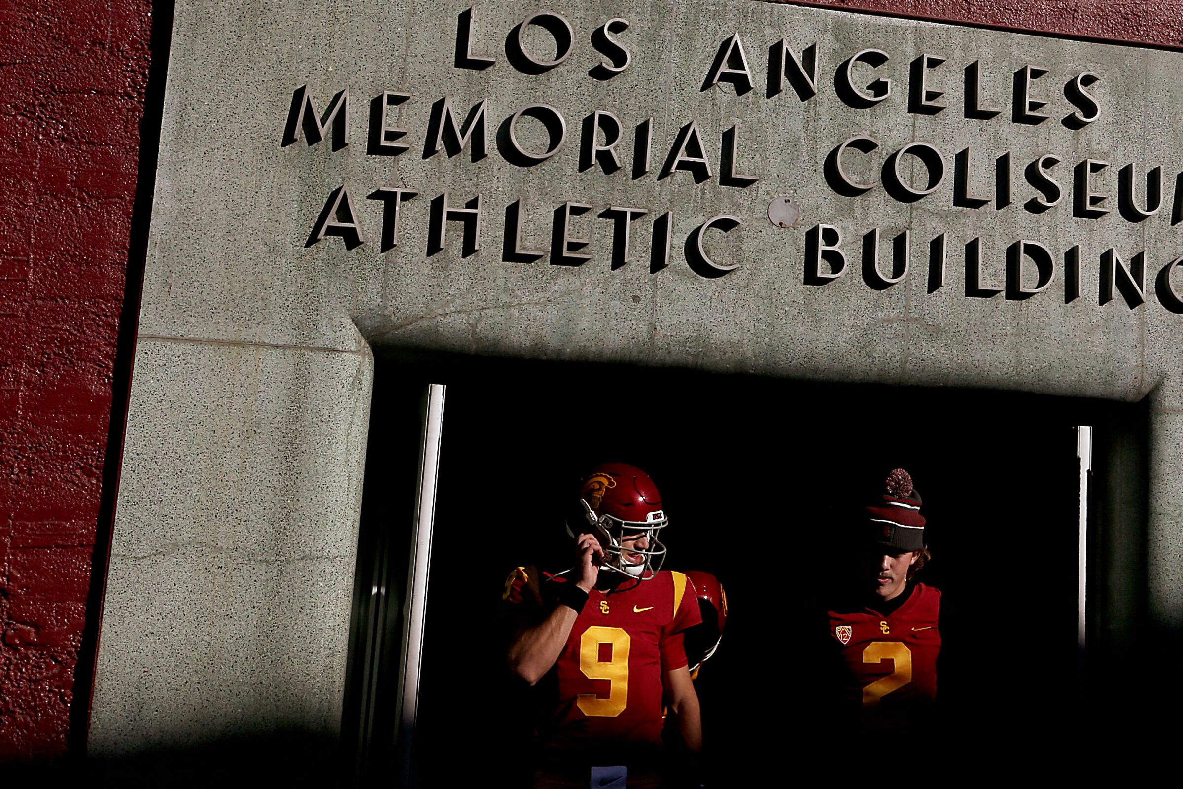 USC's Kedon Slovis and Jaxson Dart walk out of a Coliseum doorway 