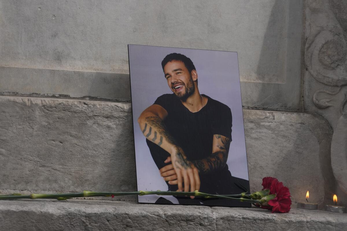 A photo of Liam Payne propped up against a concrete step with a red rose and tea light candles